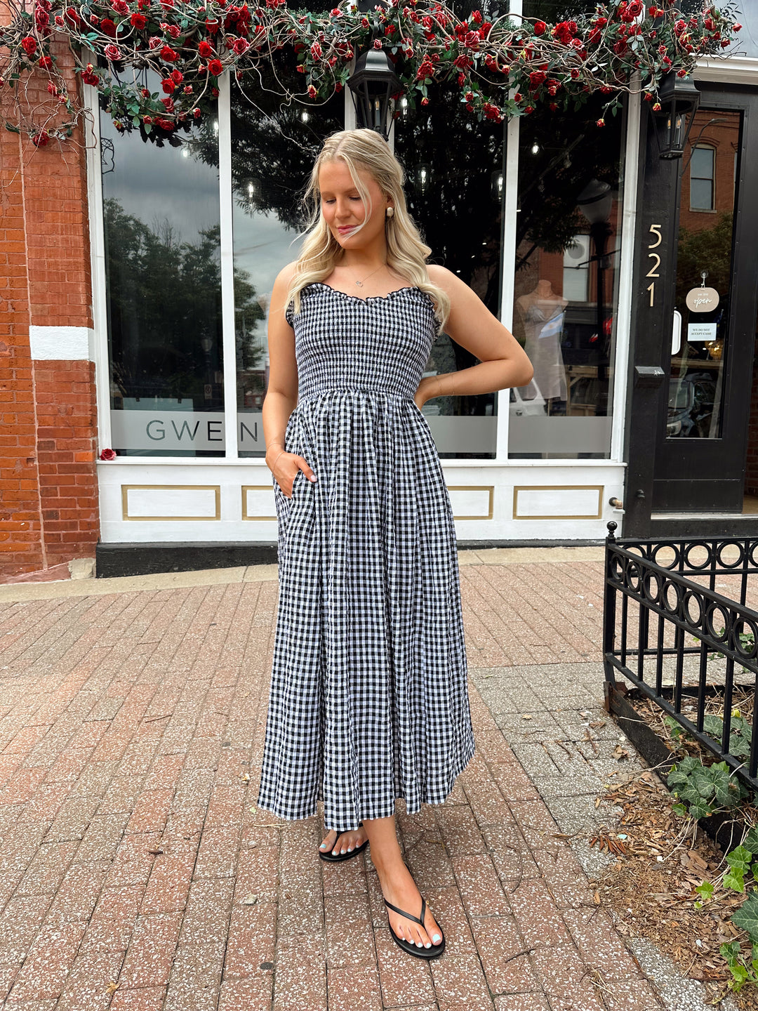 Woman wearing black and white gingham midi dress with smocked bodice and adjustable straps.