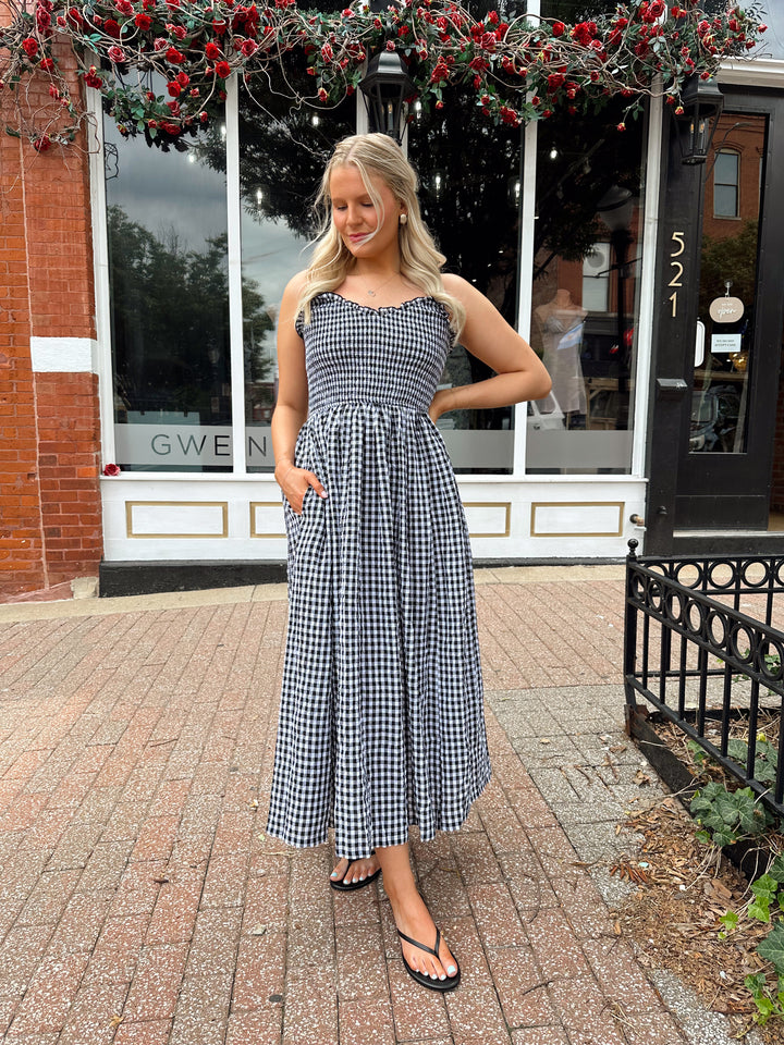 Woman wearing black and white gingham midi dress with smocked bodice and adjustable straps.
