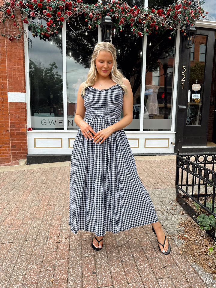 Woman wearing black and white gingham midi dress with smocked bodice and adjustable straps.