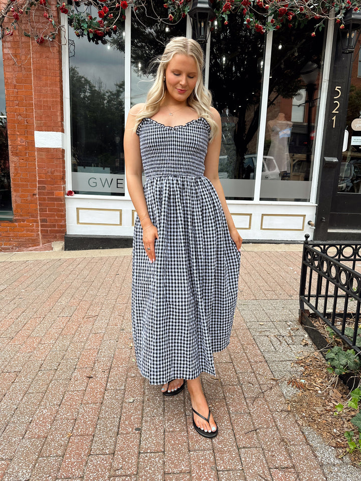 Woman wearing black and white gingham midi dress with smocked bodice and adjustable straps.