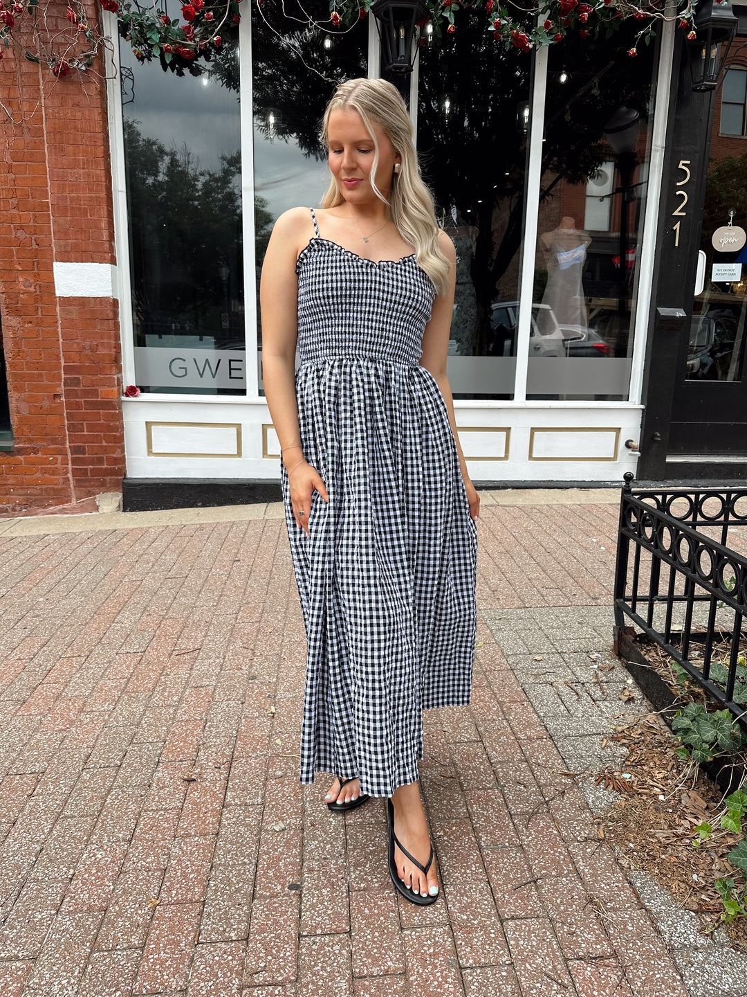 Woman wearing black and white gingham midi dress with smocked bodice and adjustable straps.