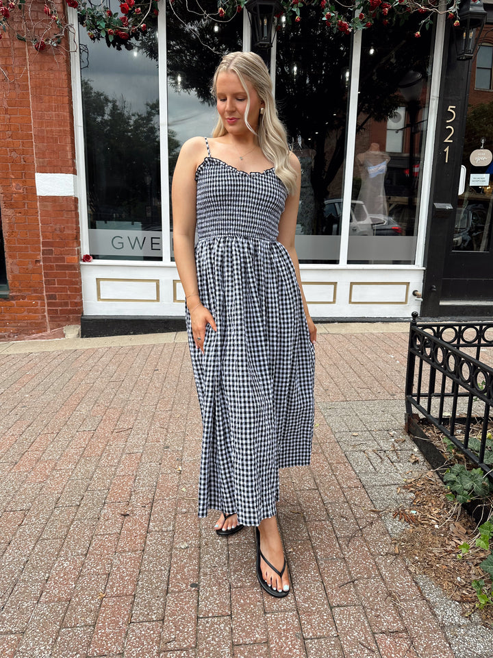Woman wearing black and white gingham midi dress with smocked bodice and adjustable straps.