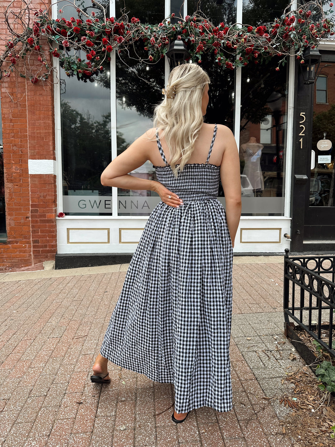Woman wearing black and white gingham midi dress with smocked bodice and adjustable straps.