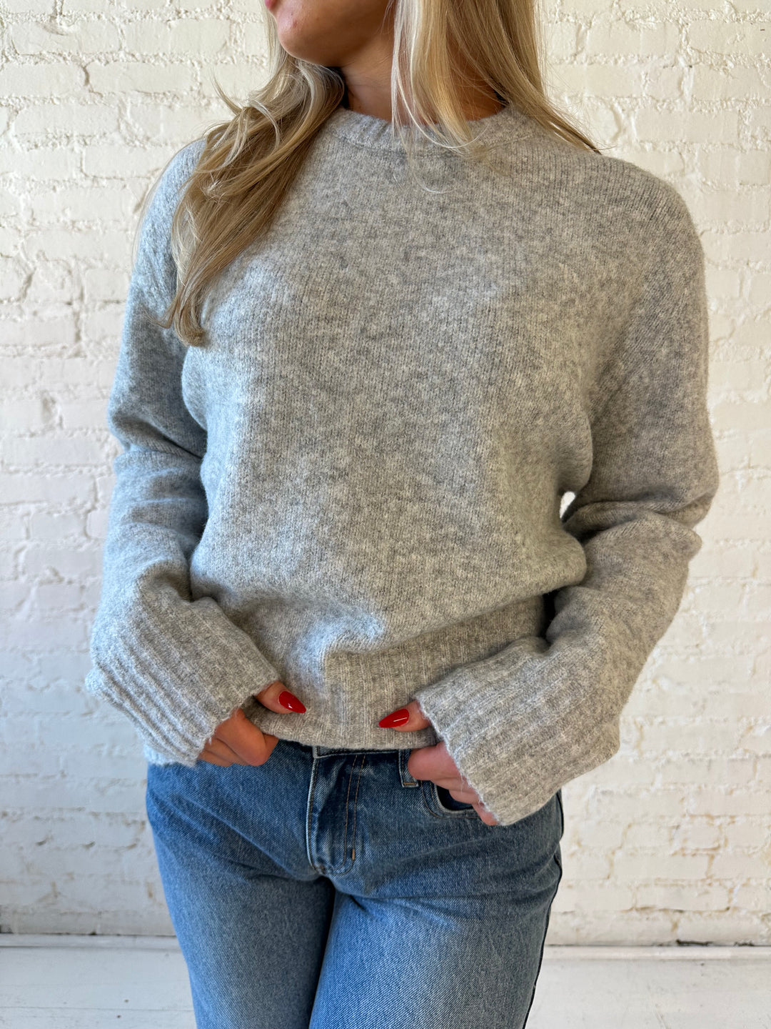 Woman wearing darker grey knit crewneck sweater with medium wash wide leg jeans. 