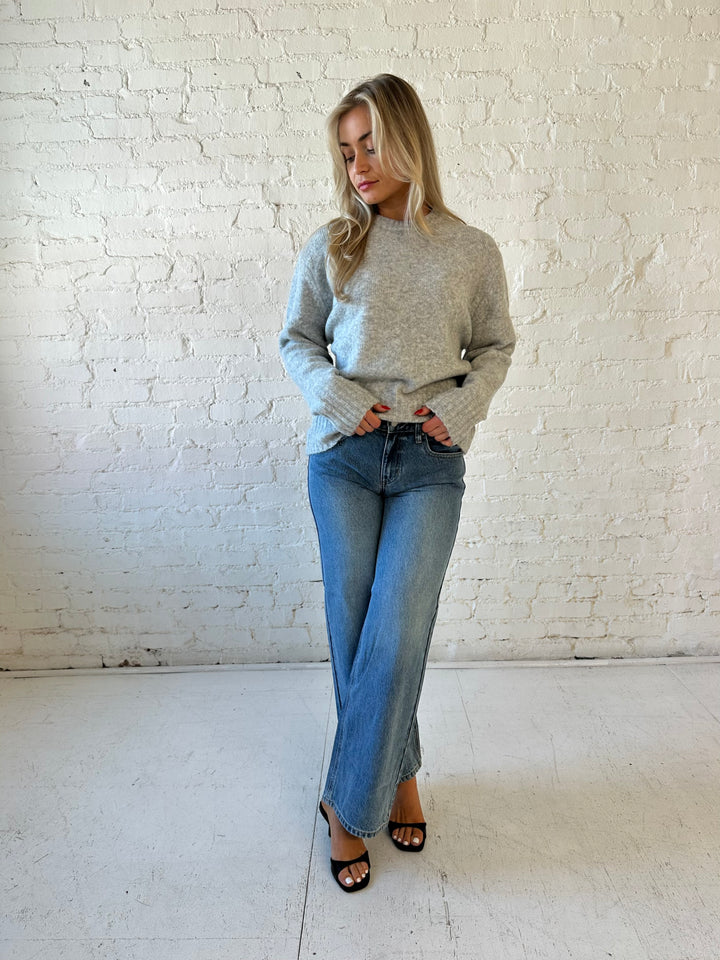 Woman wearing darker grey knit crewneck sweater with medium wash wide leg jeans. 