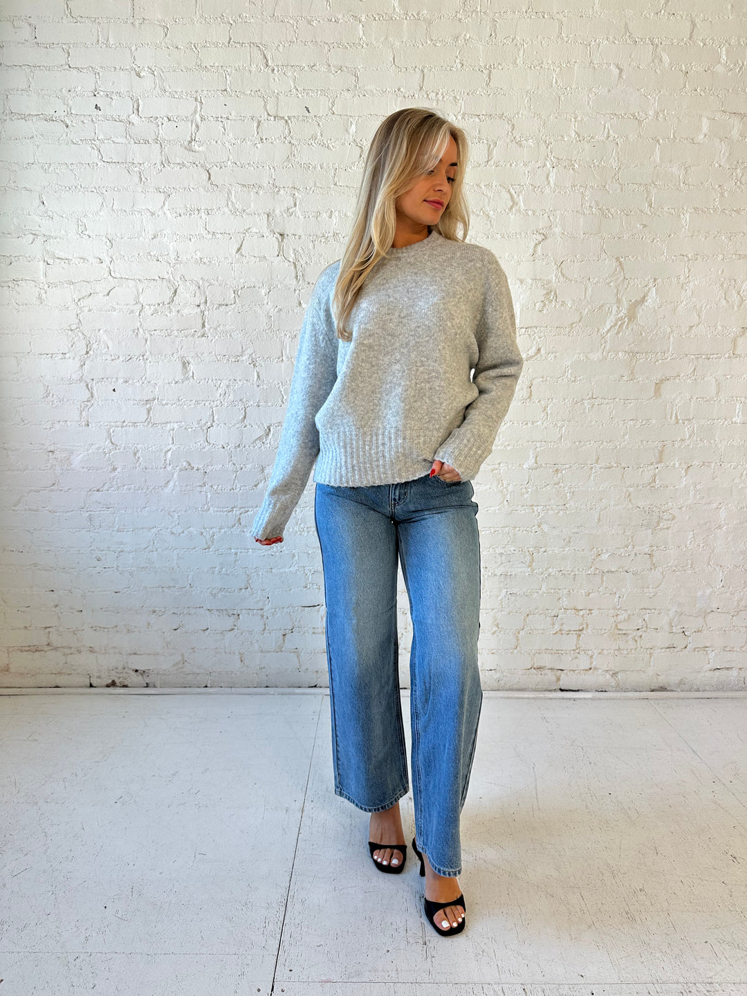 Woman wearing darker grey knit crewneck sweater with medium wash wide leg jeans. 