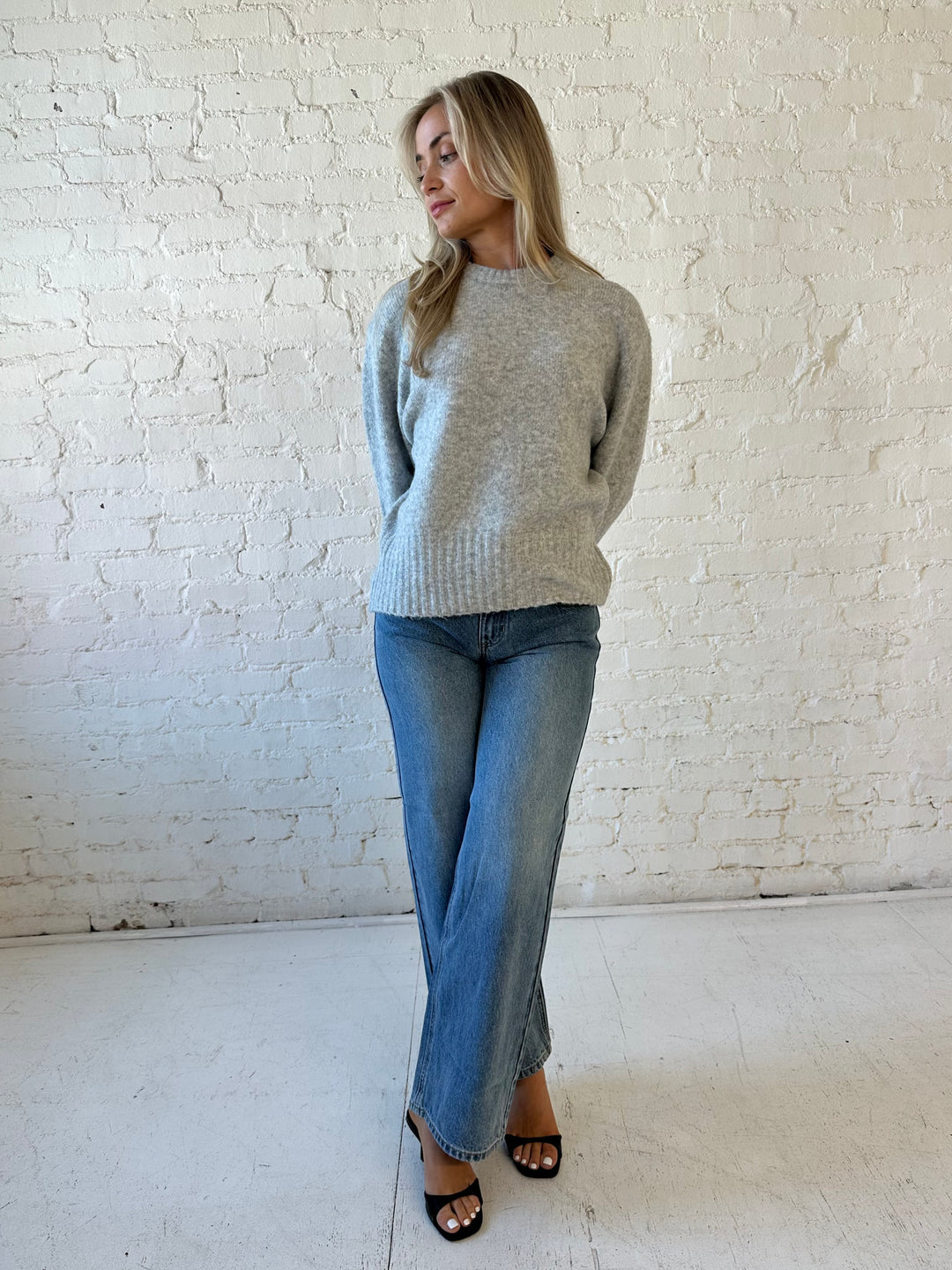 Woman wearing darker grey knit crewneck sweater with medium wash wide leg jeans. 