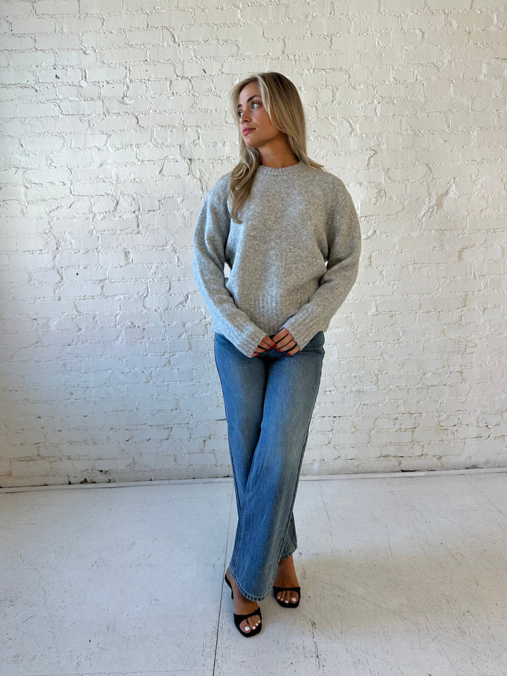 Woman wearing darker grey knit crewneck sweater with medium wash wide leg jeans. 