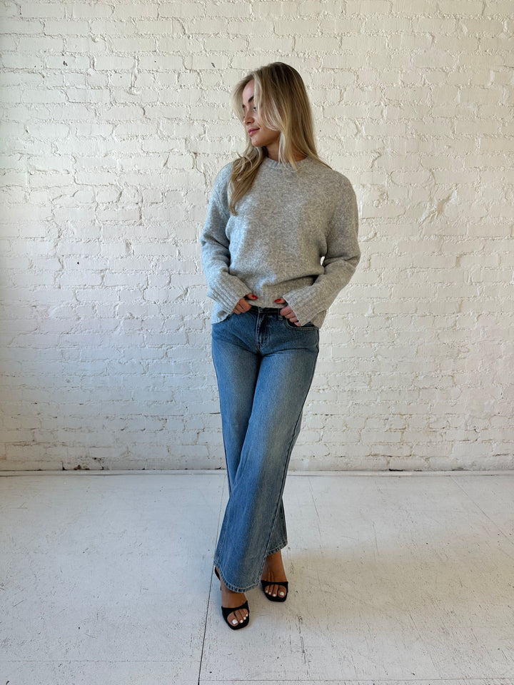 Woman wearing darker grey knit crewneck sweater with medium wash wide leg jeans. 
