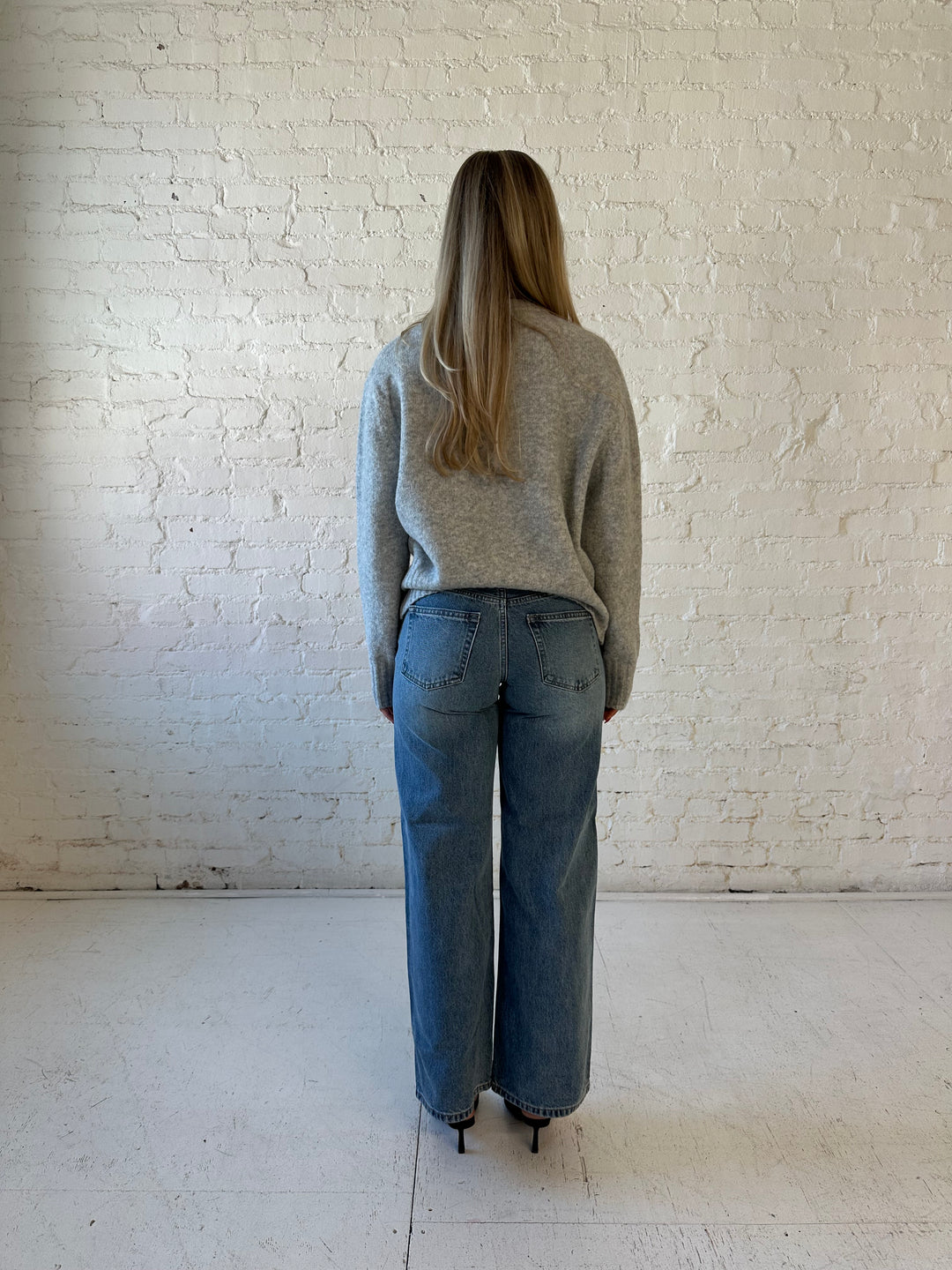 Woman wearing darker grey knit crewneck sweater with medium wash wide leg jeans. 