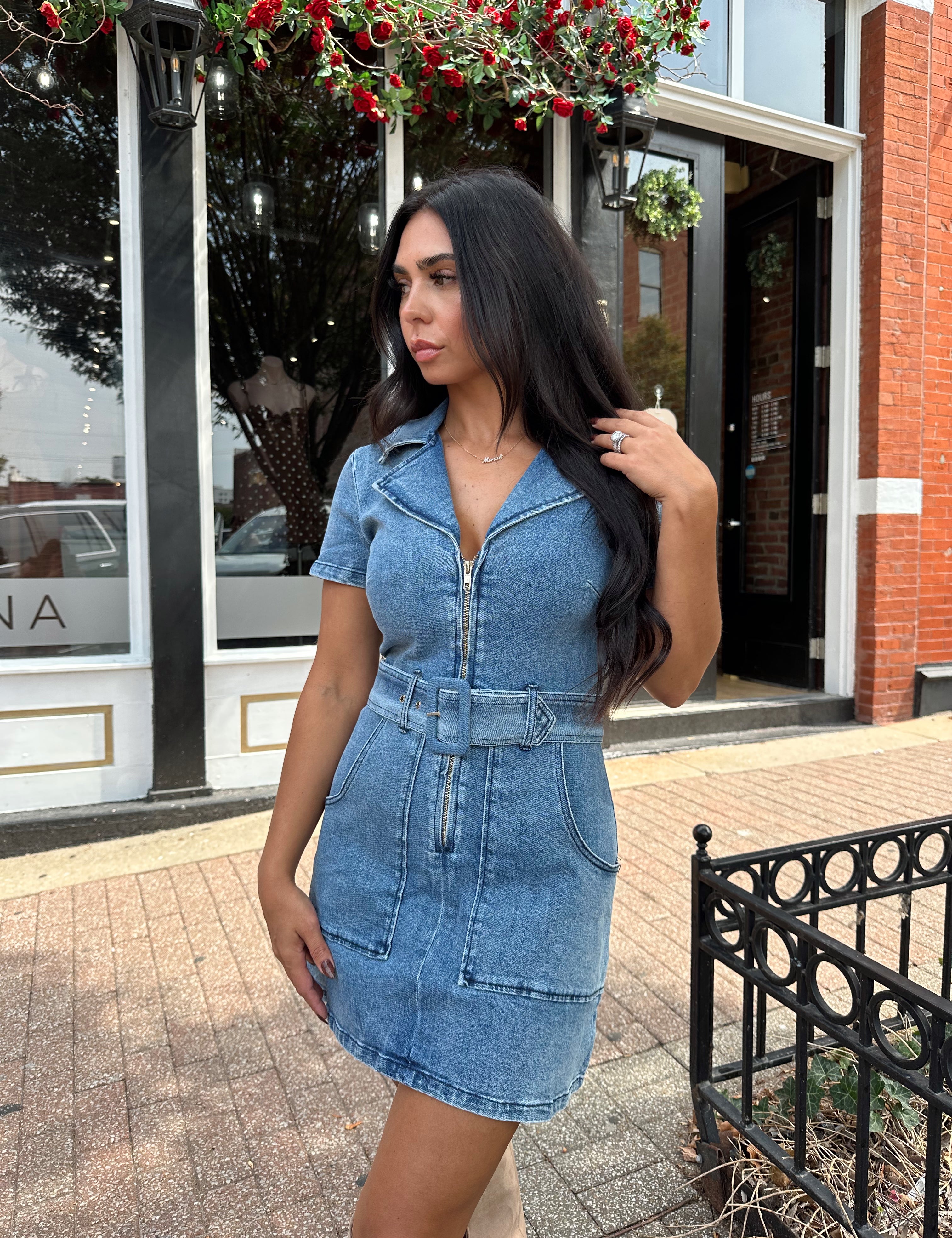 Woman wearing light wash denim mini dress with belt detail and collar neckline.