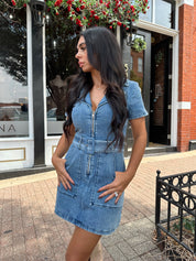 Woman wearing light wash denim mini dress with belt detail and collar neckline.