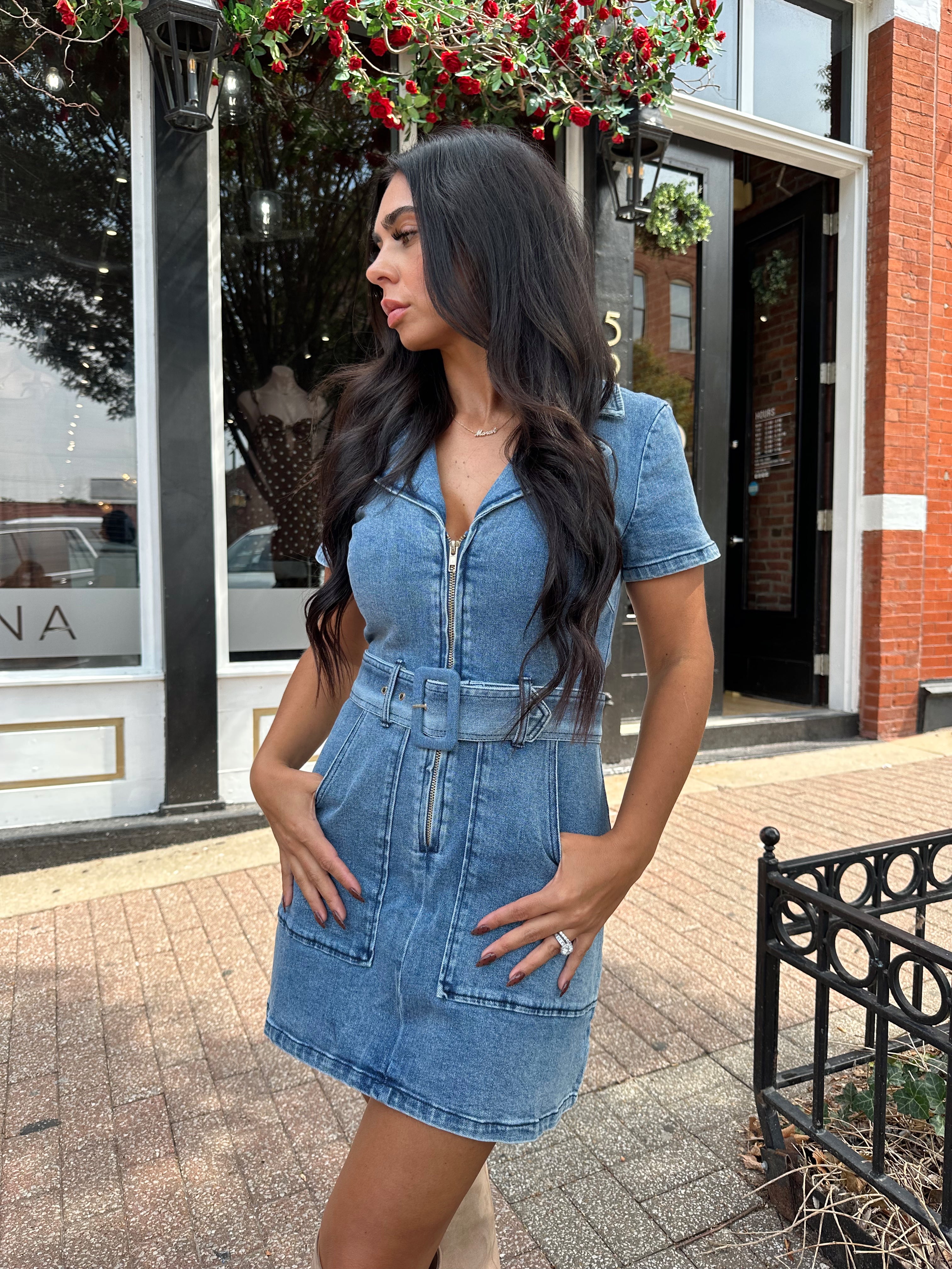 Woman wearing light wash denim mini dress with belt detail and collar neckline.