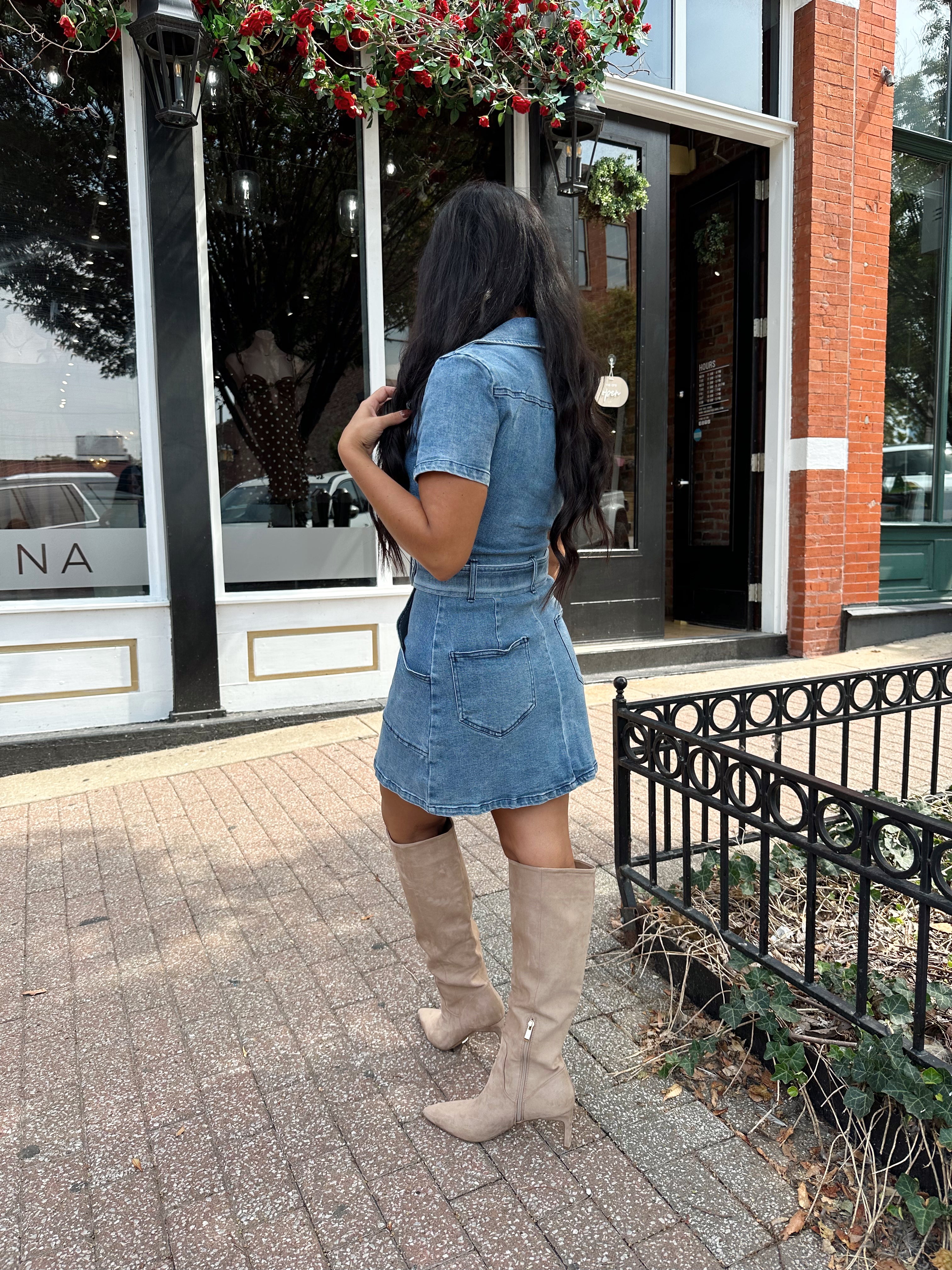 Woman wearing light wash denim mini dress with belt detail and collar neckline.