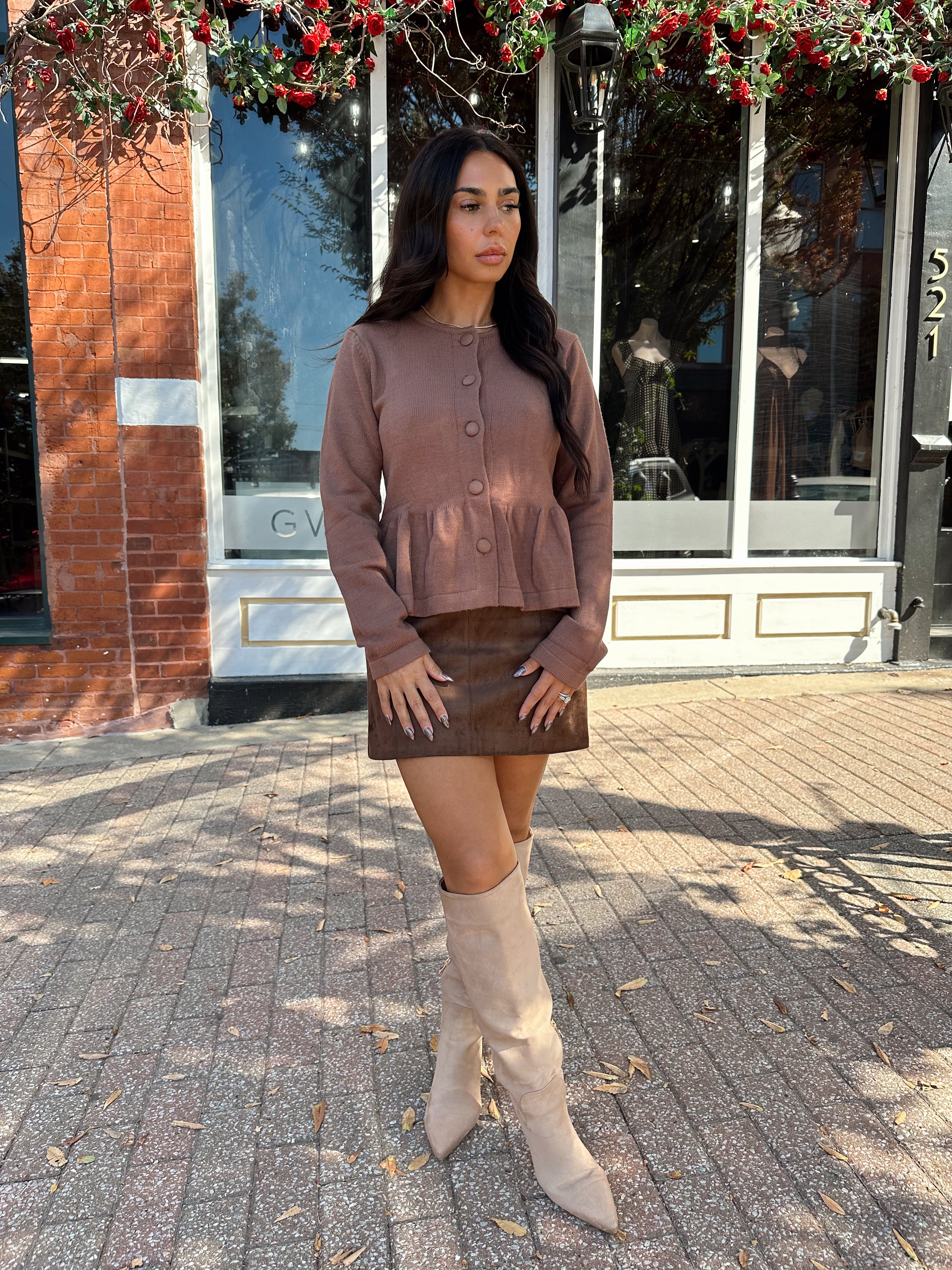 Woman wearing brown peplum style sweater top with button closure. 
