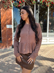 Woman wearing brown peplum style sweater top with button closure. 