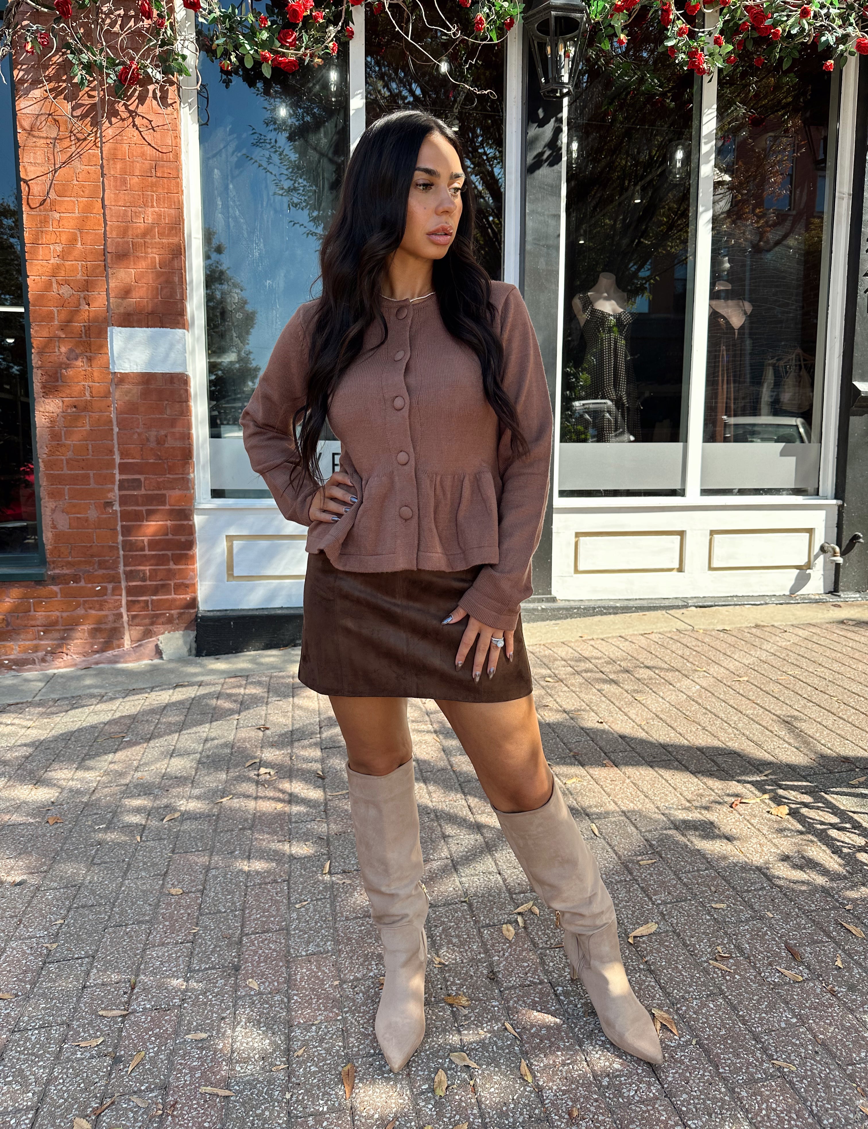 Woman wearing brown peplum style sweater top with button closure. 