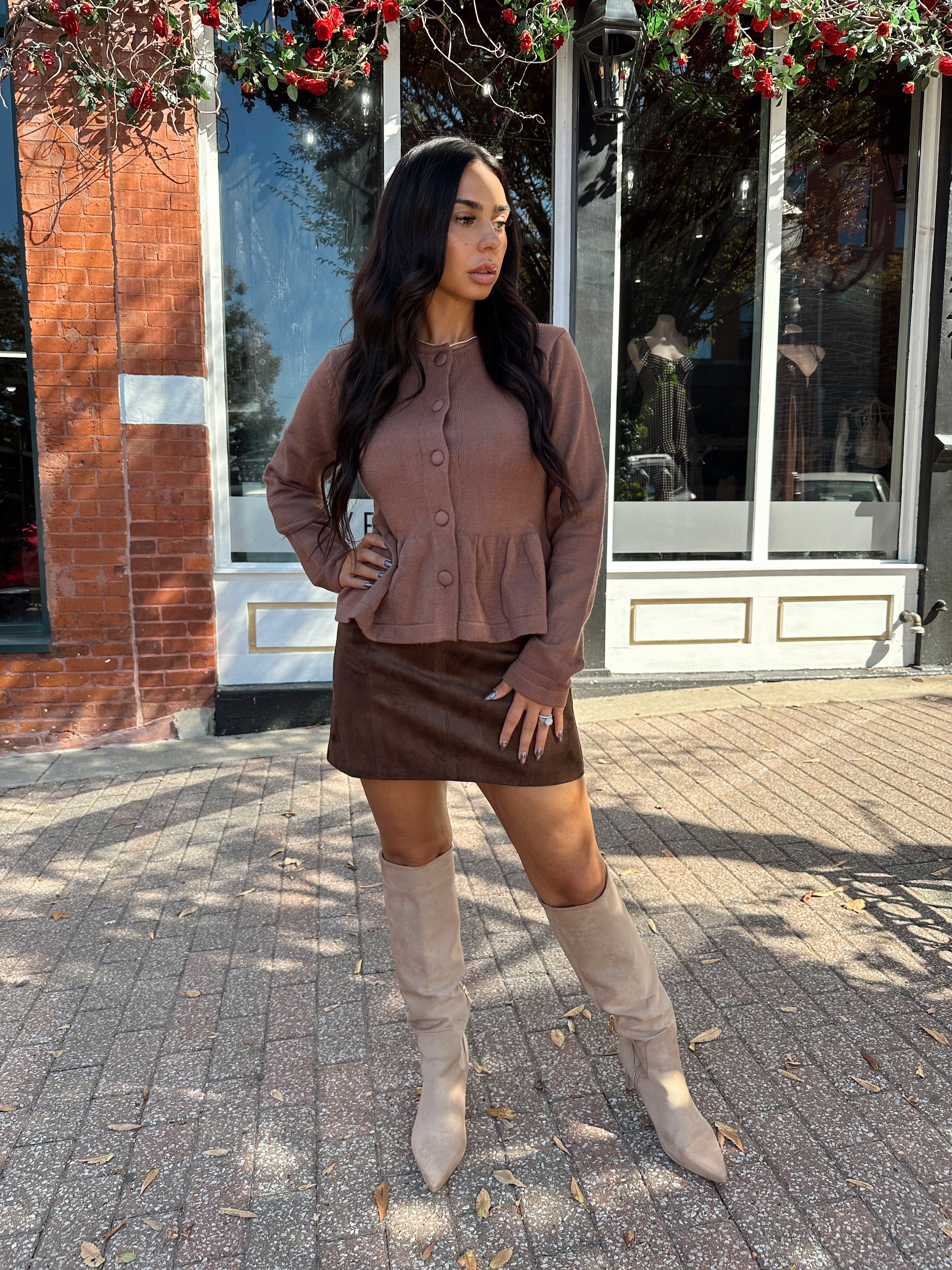 Woman wearing brown peplum style sweater top with button closure. 