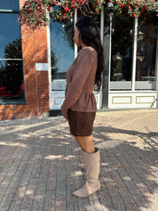 Woman wearing brown peplum style sweater top with button closure. 