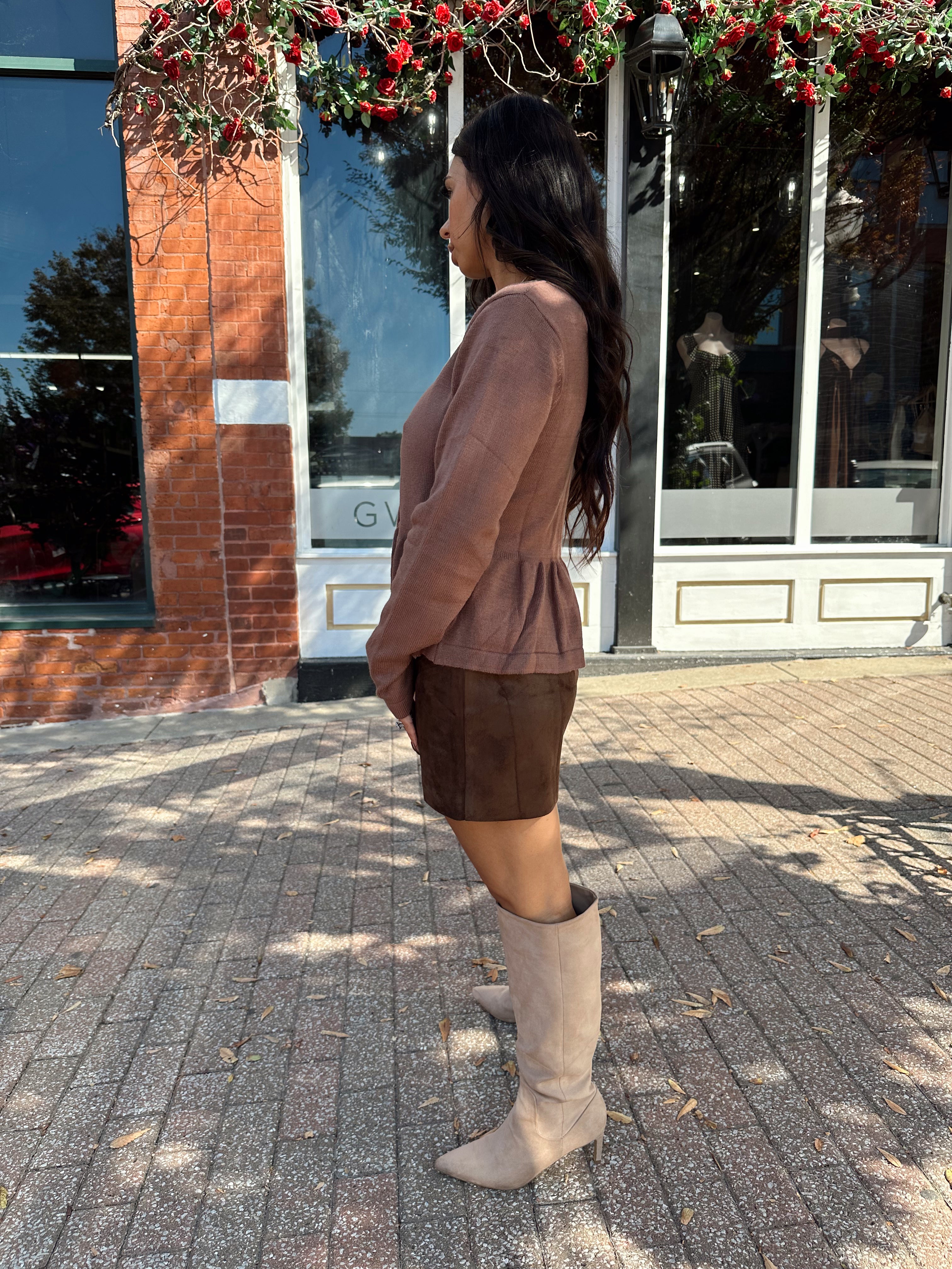 Woman wearing brown peplum style sweater top with button closure. 