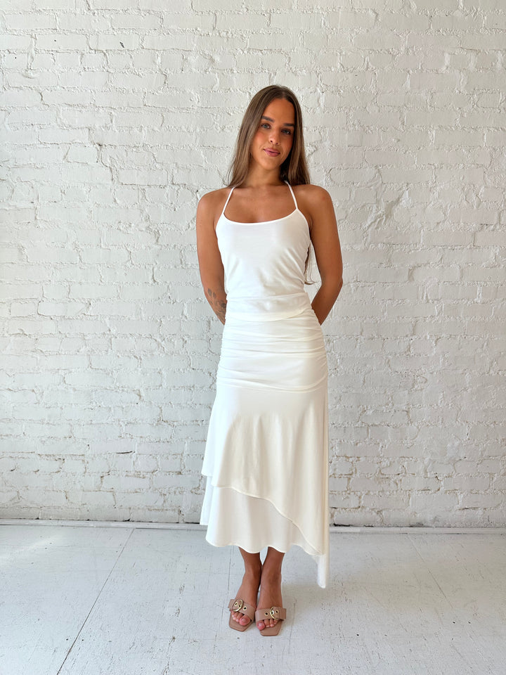 Woman wearing white two piece set with layered midi skirt, and halter top. 