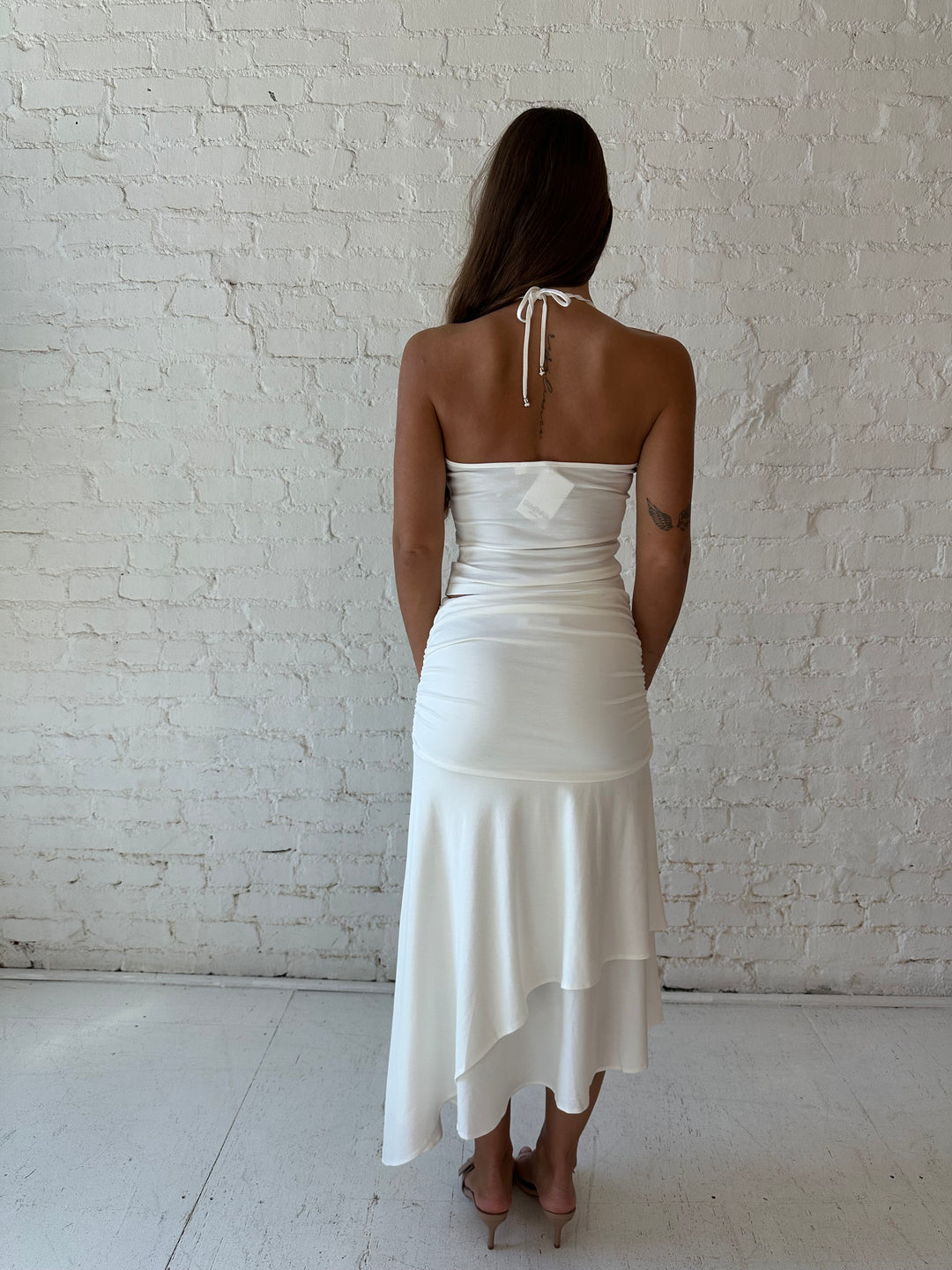 Woman wearing white two piece set with layered midi skirt, and halter top. 