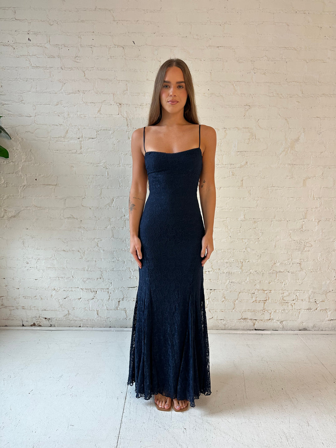 Woman wearing navy blue lace maxi dress with open back, and clasp back strap.