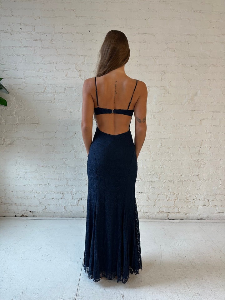 Woman wearing navy blue lace maxi dress with open back, and clasp back strap.