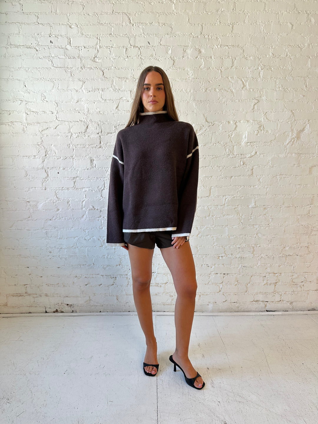 Woman wearing dark brown faux leather pleated shorts and a boxy oversized sweater.
