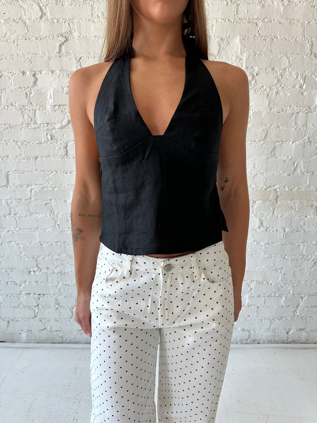 Woman wearing black linen halter top with white polka dot low rise jeans. 