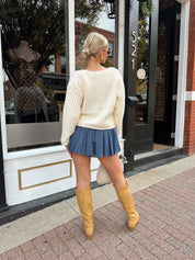 Woman wearing ivory knit front tie cardigan with functional pockets overtop dusty blue mini dress.