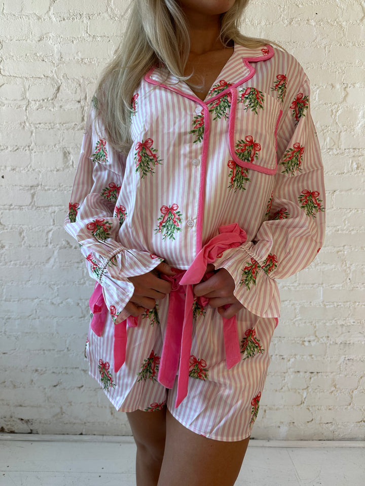 Woman wearing light pink striped satin pajamas with little green wreaths all over. 