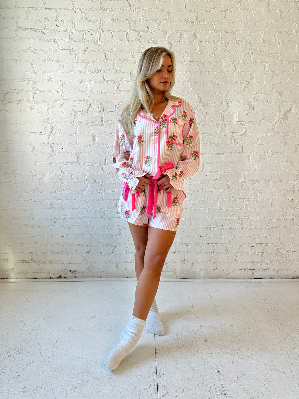 Woman wearing light pink striped satin pajamas with little green wreaths all over. 