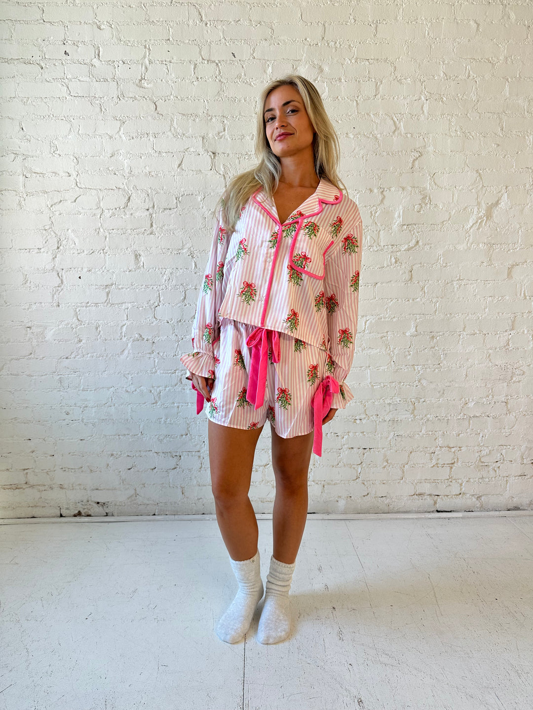 Woman wearing light pink striped satin pajamas with little green wreaths all over. 