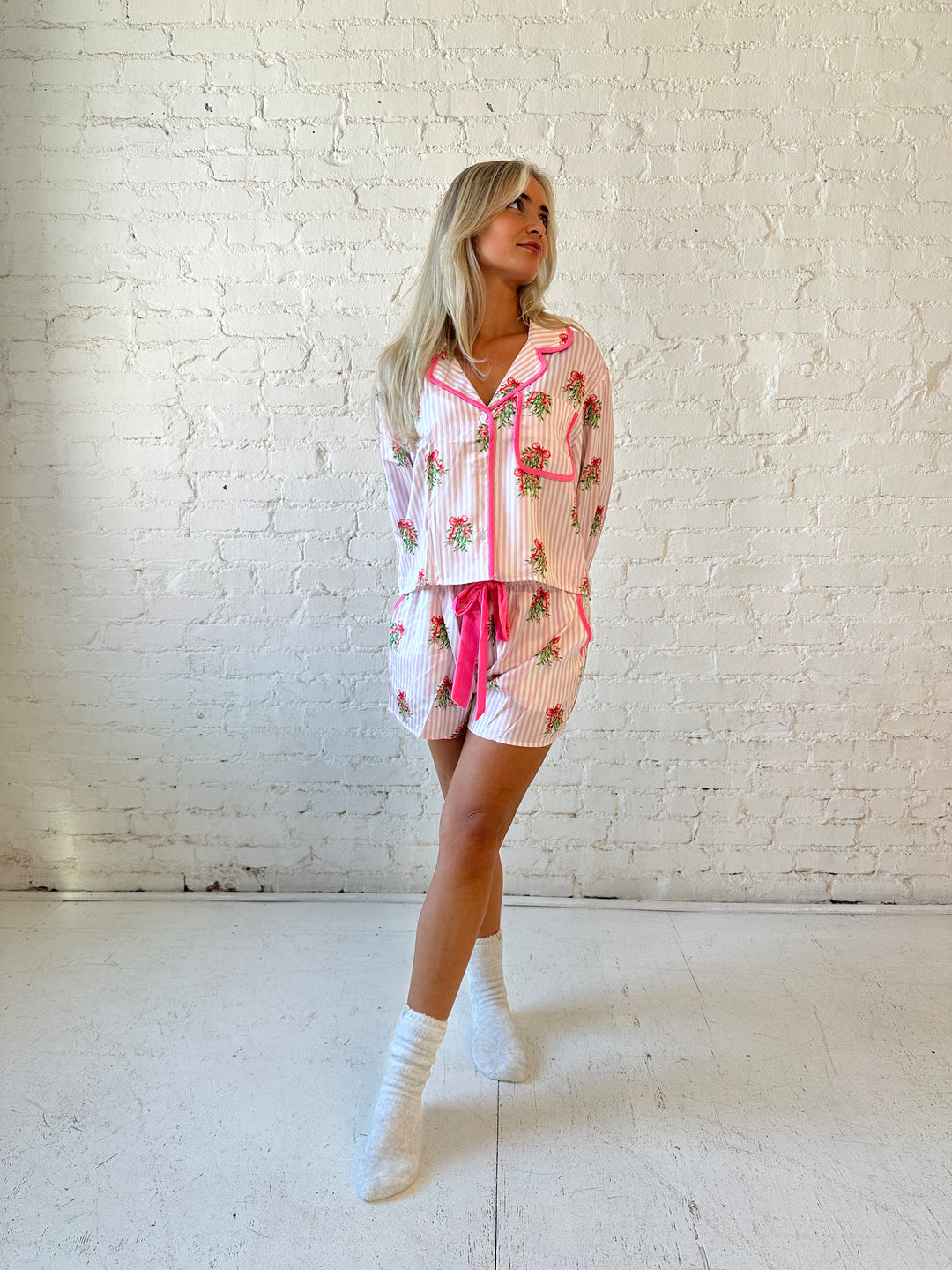 Woman wearing light pink striped satin pajamas with little green wreaths all over. 