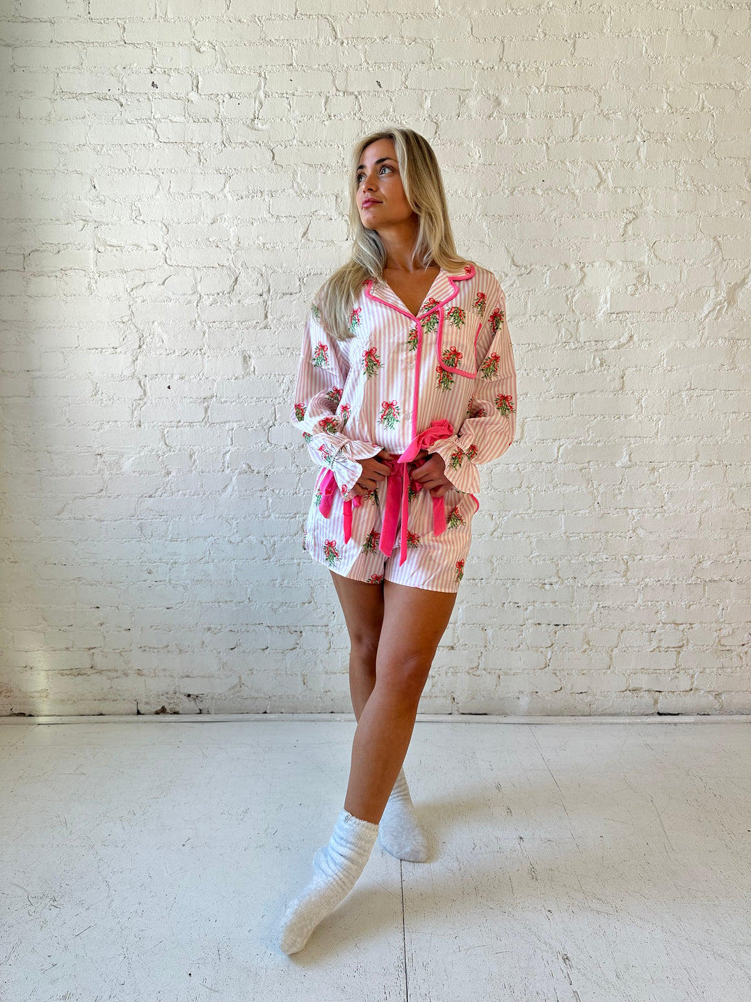 Woman wearing light pink striped satin pajamas with little green wreaths all over. 