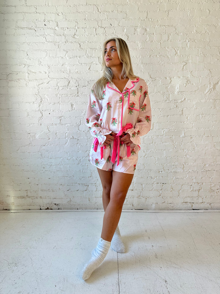 Woman wearing light pink striped satin pajamas with little green wreaths all over. 