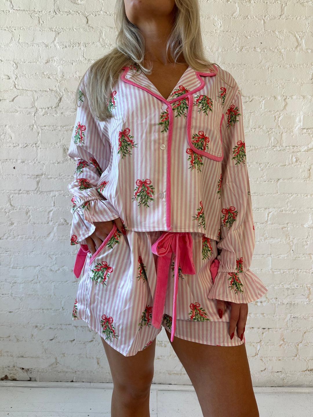 Woman wearing light pink striped satin pajamas with little green wreaths all over. 