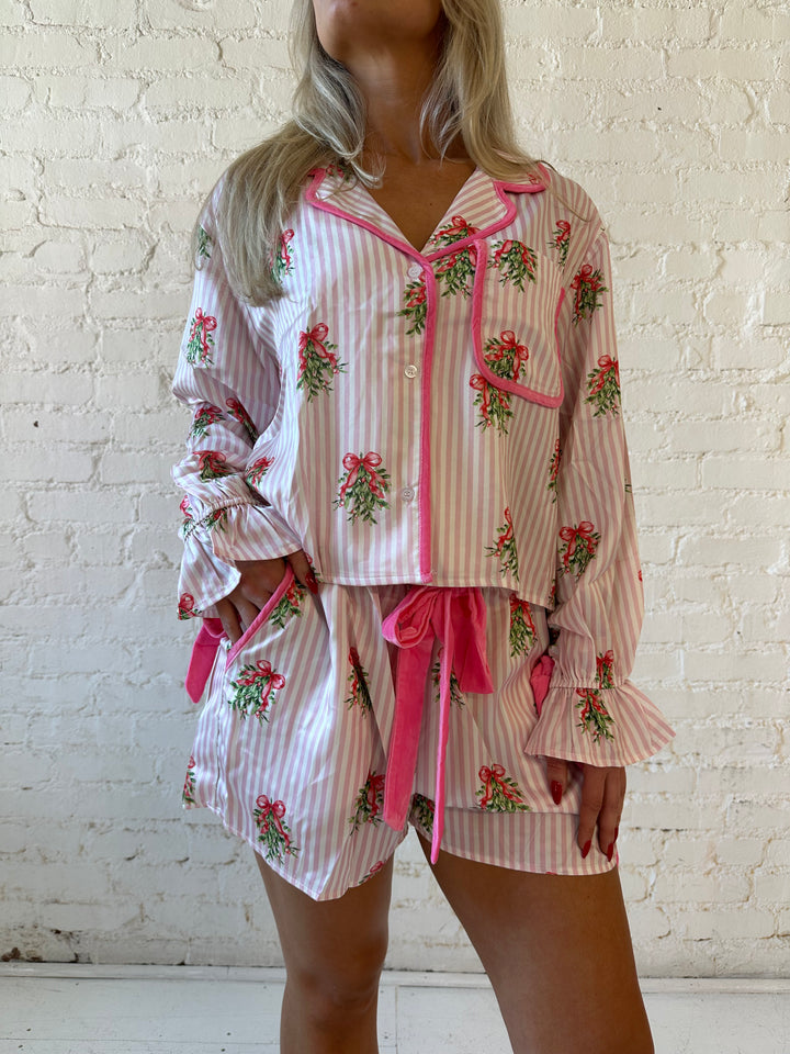 Woman wearing light pink striped satin pajamas with little green wreaths all over. 