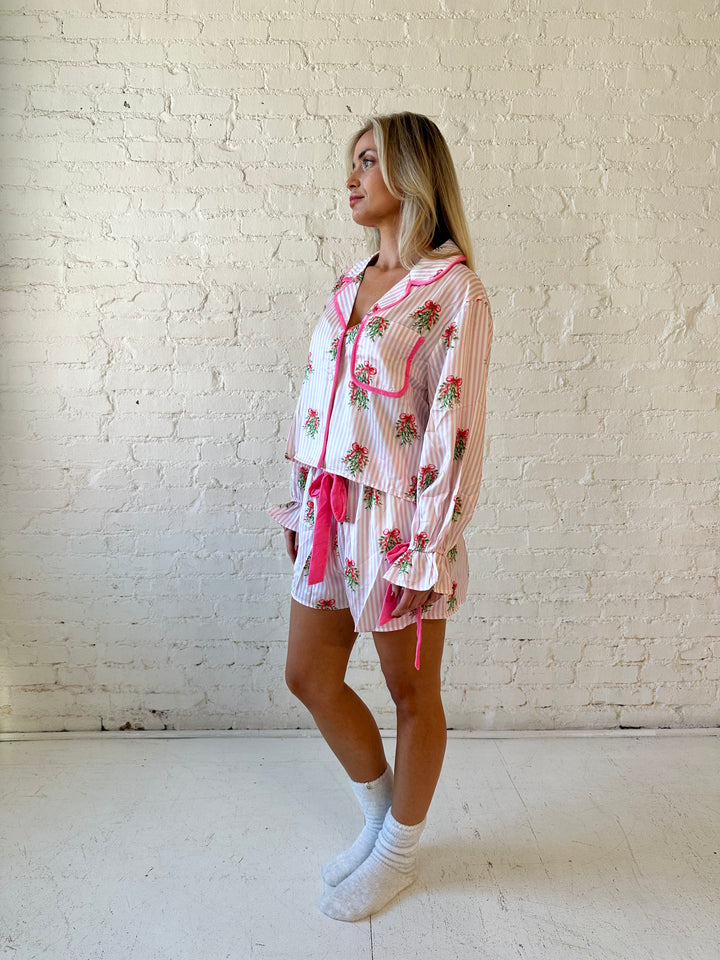 Woman wearing light pink striped satin pajamas with little green wreaths all over. 