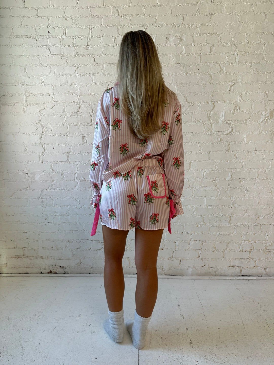 Woman wearing light pink striped satin pajamas with little green wreaths all over. 