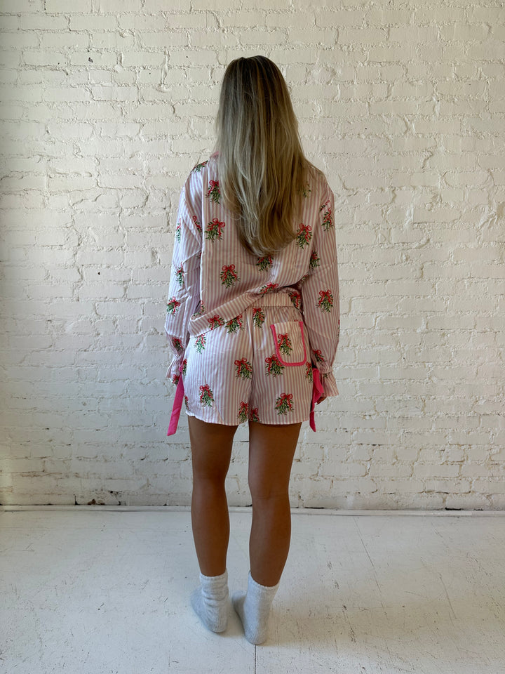 Woman wearing light pink striped satin pajamas with little green wreaths all over. 
