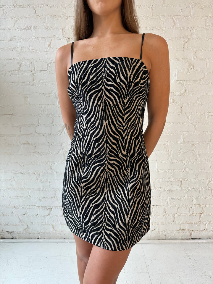 Woman wearing zebra print shift style mini dress with black spaghetti straps, and heels.