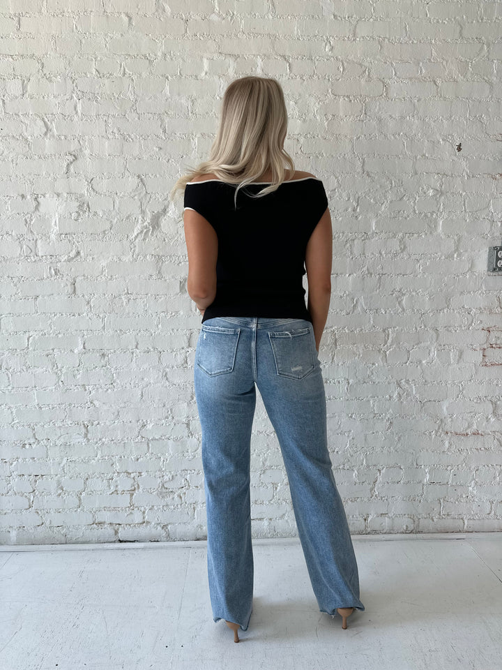 Woman wearing black knit off the shoulder top with white contrast trim and distressed jeans.