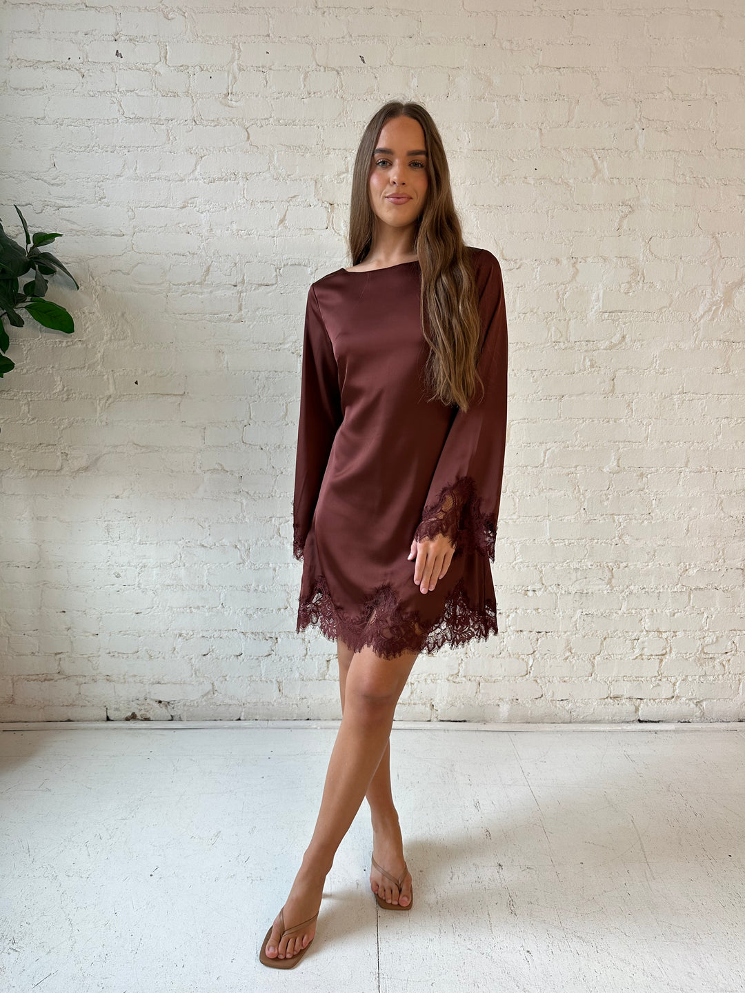 Woman wearing rust satin mini dress with long sleeves and lace trim detail.