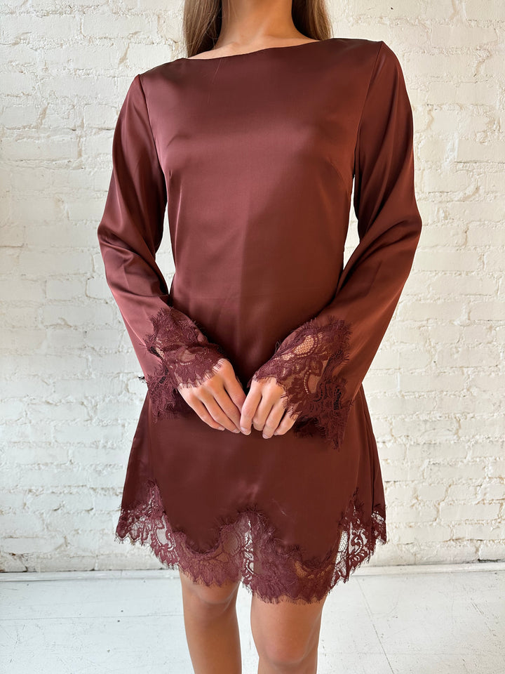 Woman wearing rust satin mini dress with long sleeves and lace trim detail.