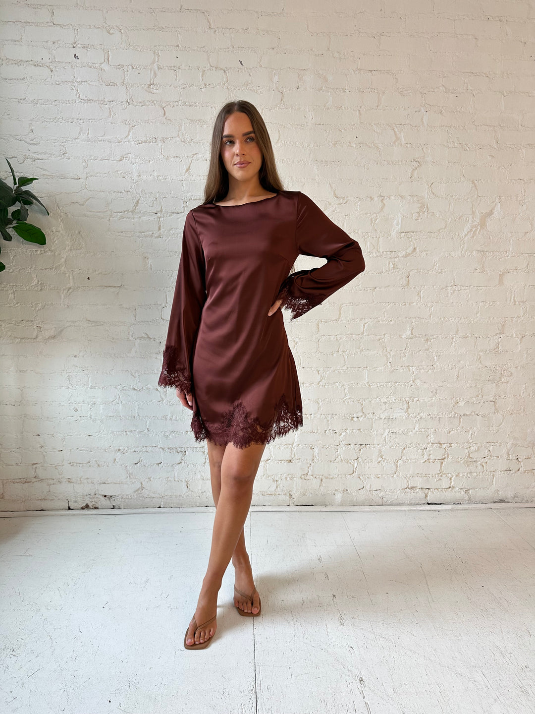 Woman wearing rust satin mini dress with long sleeves and lace trim detail.
