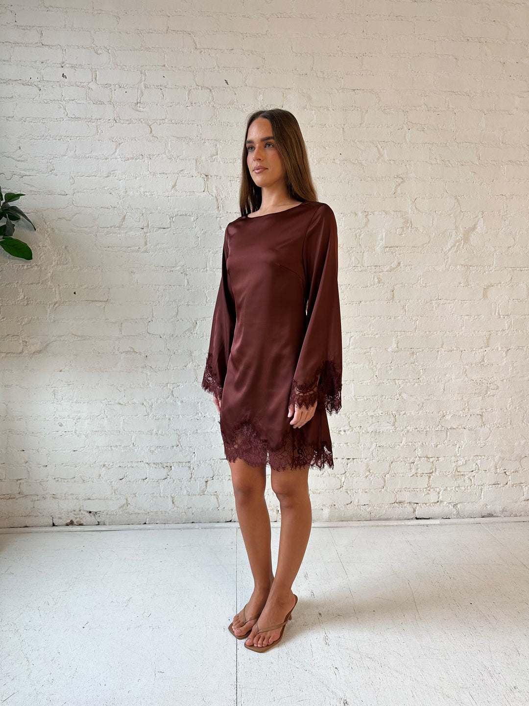 Woman wearing rust satin mini dress with long sleeves and lace trim detail.