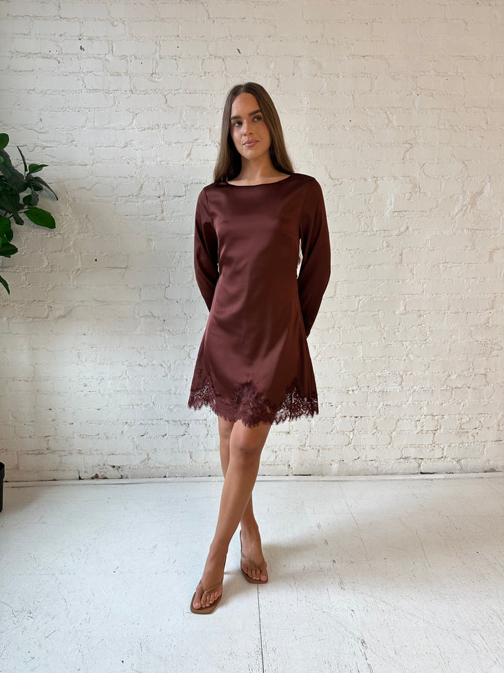 Woman wearing rust satin mini dress with long sleeves and lace trim detail.