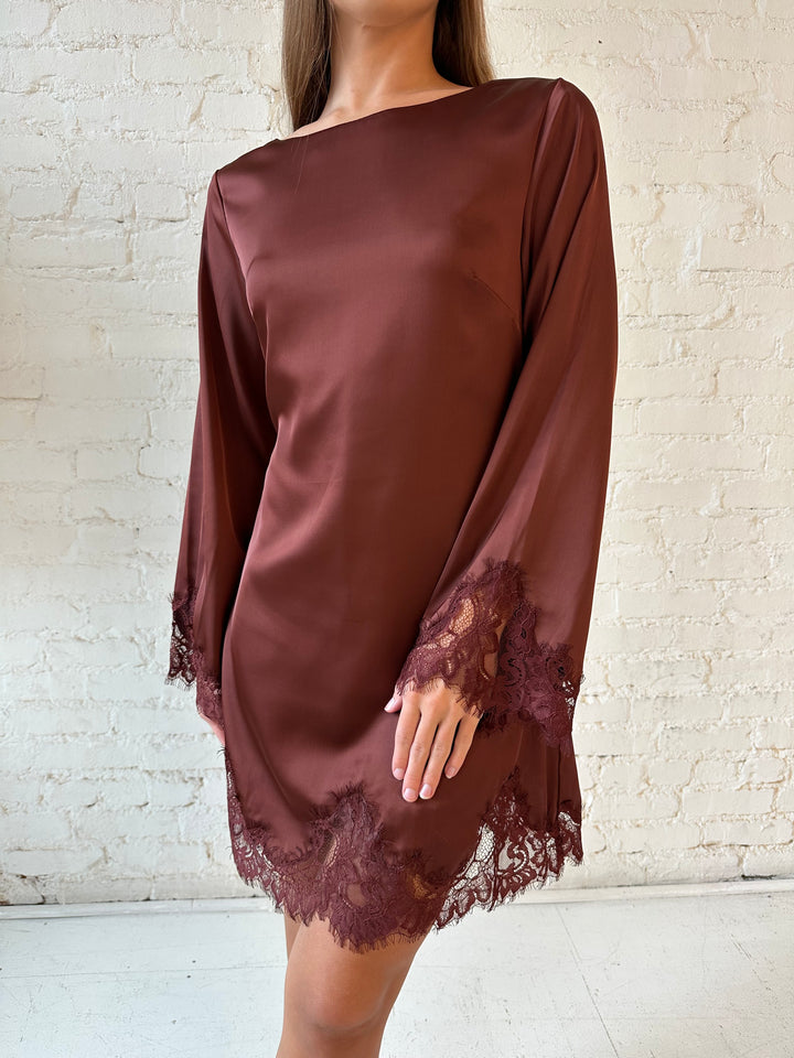 Woman wearing rust satin mini dress with long sleeves and lace trim detail.